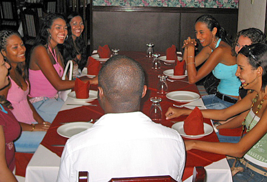A Black man dines with a group of Colombian women in a restaurant, all smiling and sharing friendly conversation