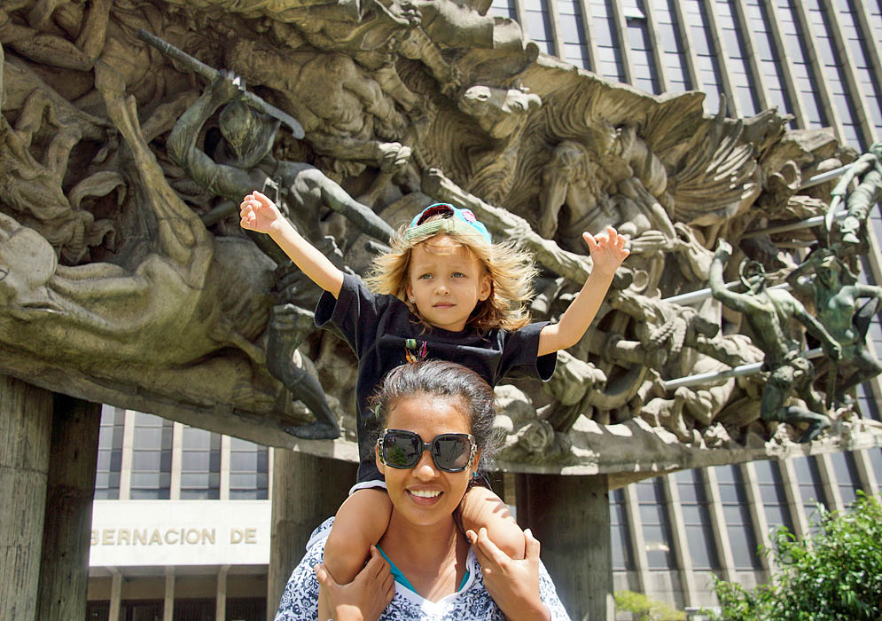 Girl on top of mom's shoulder in front of statue