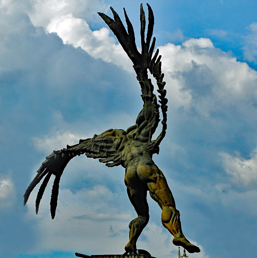 A statue of the back of a man with wing under blue sky