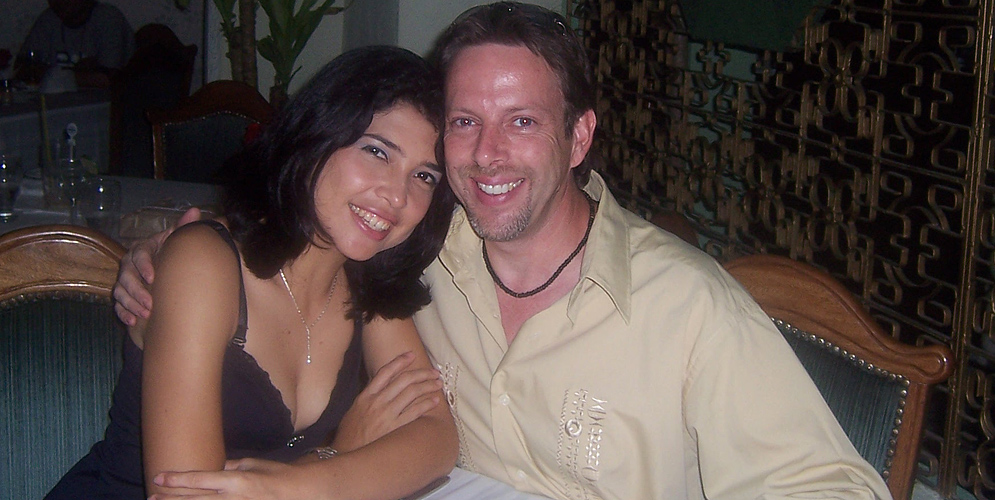 Hombre extranjero con mujer colombiana sentados juntos, él con el brazo sobre su hombro, ejemplo de buscar pareja seria con agencia matrimonial internacional