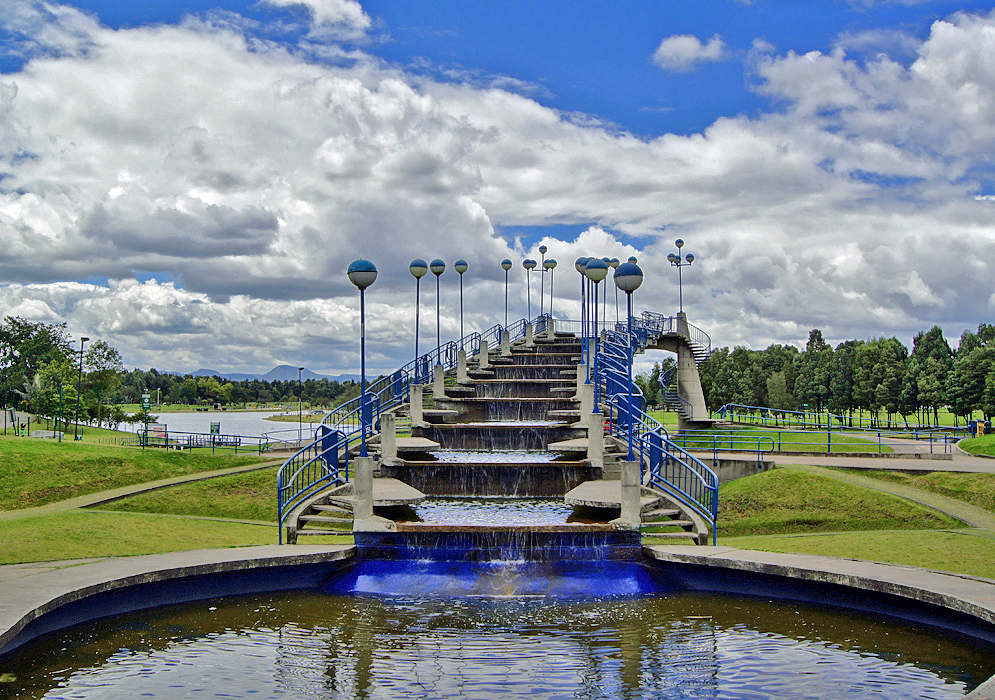 A Bogotá park with a cascading fountain and a lake in the background