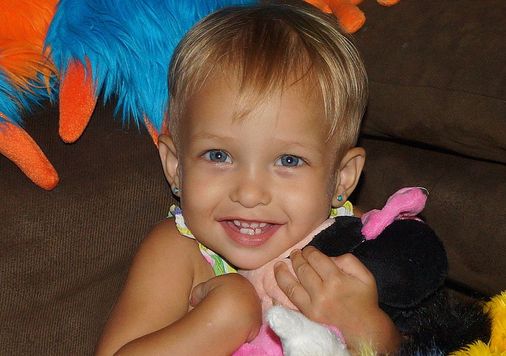 Beautiful blond 1 year old Colombian American girl smiling while holding Mini Mouse close to her heart