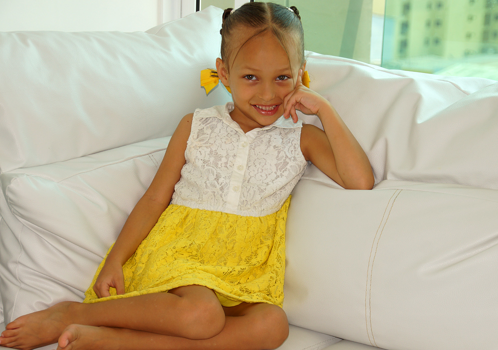 Attractive Colombian American girl rest on a white sofa with a yellow summer dress