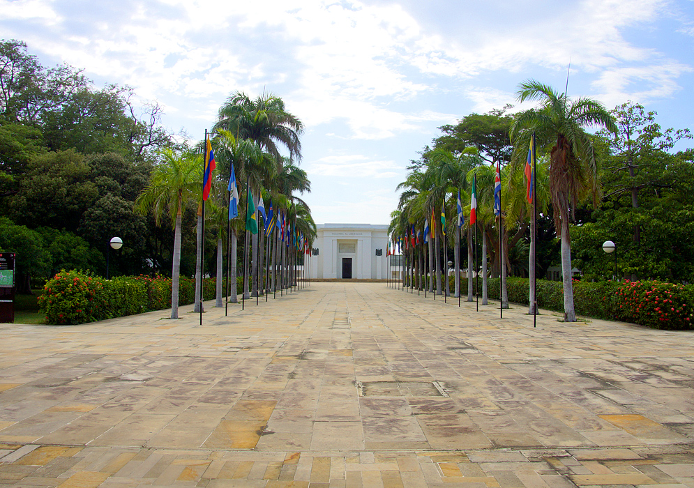 A white memorial for Simón Bolívar in between a row of flags and palm trees