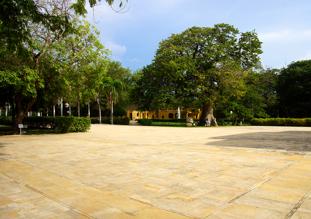 A large stone-colored courtyard with flags and yellow buildings in the background