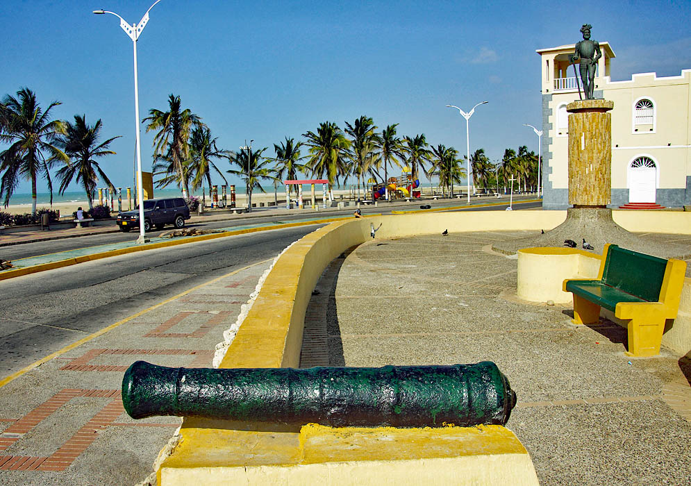 Main street Riohacha with a canon, statue, church, palm trees, beach and ocean