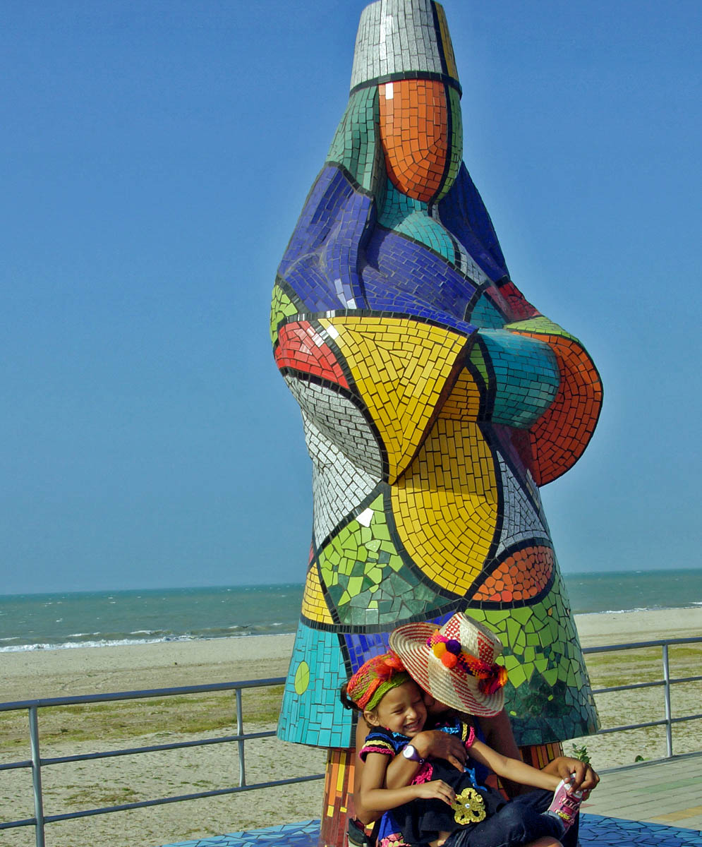 Colombian mom hugging her happy young daughter in front of a colorful tile statue honoring the Wayuu indians