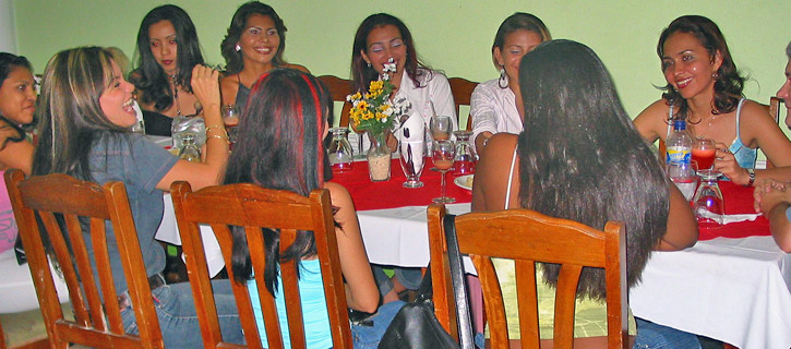 A man is introduced to a table of Colombian women in a bright dining room with flowers and cocktails during our group meeting