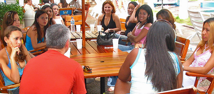 One man meets a group of smiling Colombian women around an outdoor wooden table during our introductions social