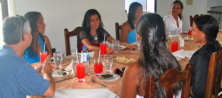 A man sits with several Colombian women at a restaurant table with red drinks during a relaxed lunch-style introductions meeting