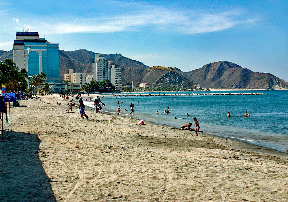 Beach with a with few people during dry season with mountains and a couple of hotels 