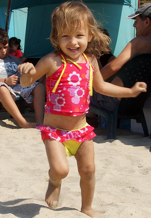 Niña colombo amer yficana con un vestido de baño rojo y amarillo, corriendo por la playa