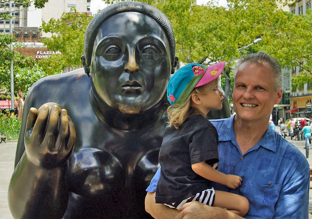 Three year old girl leaning to kiss the cheek of her dad in front of a Botero statue