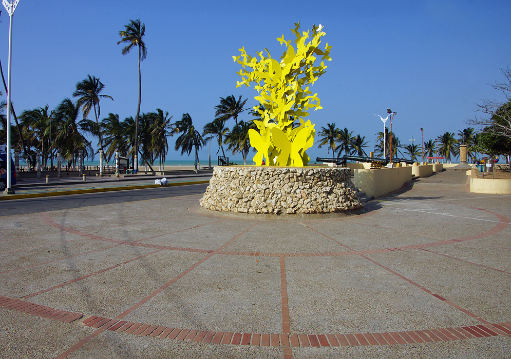 A statue of yellow butterflies with canons and palm trees and caribean in the background under blue skies