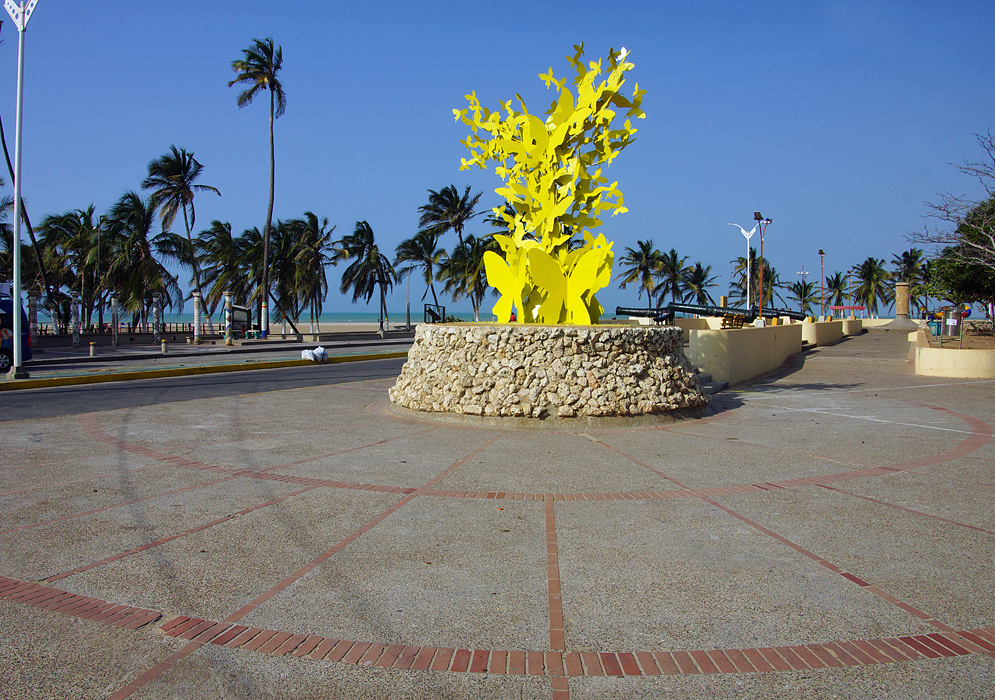 A statue of yellow butterflies with canons and palm trees and caribean in the background under blue skies
